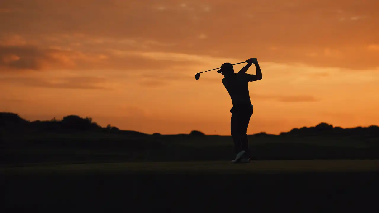 A golfer silhouetted at the top of the backswing at sunset